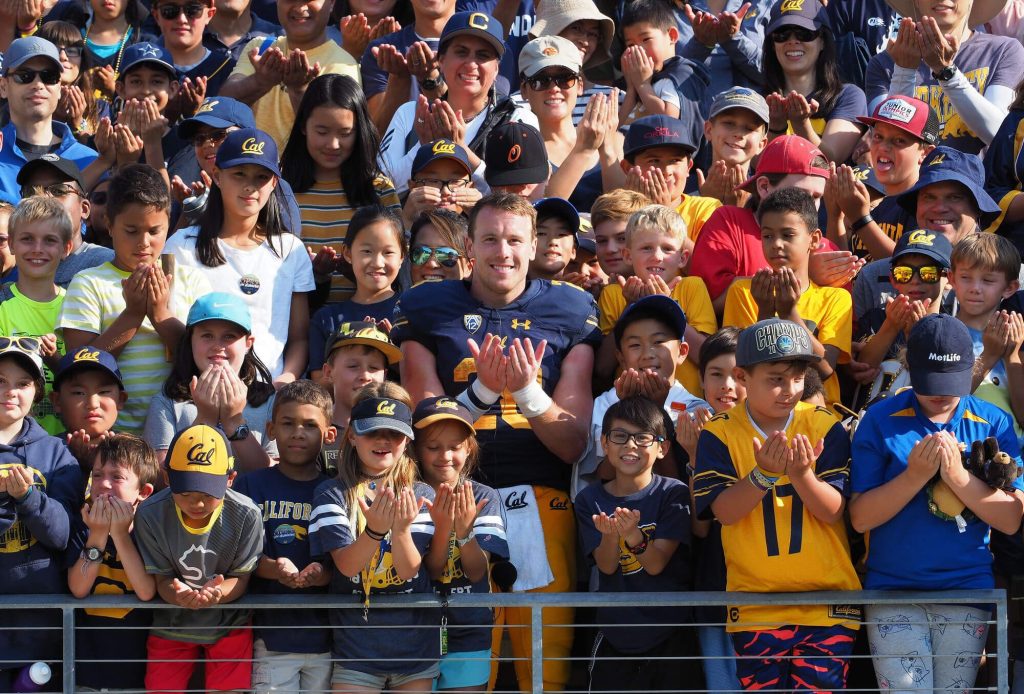 Patrick in a crowd of children, all holding their hands out as though they're holding books